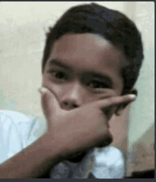 a young boy covering his mouth with his hand while looking at the camera