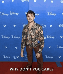 a man in a floral shirt is standing on a red carpet in front of a disney wall .