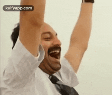 a man with a mustache is raising his arms in the air and laughing .