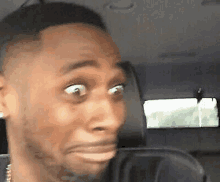 a man is sitting in the back seat of a car making a surprised face .