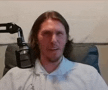 a man with long hair is sitting in a chair with a microphone in front of him .