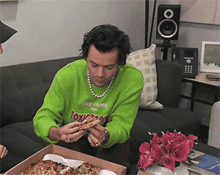 a man in a green sweater is eating pizza from a box