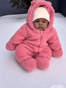 a baby wearing a pink sherpa outfit and a white hat is sitting in the snow