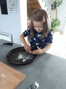 a little girl wearing a blue shirt with unicorns on it spreads flour on a tray