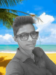 a young man wearing sunglasses and earphones is taking a selfie on a beach .