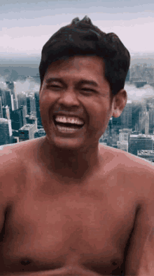 a shirtless man is laughing with a city skyline in the background