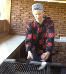 a young man wearing a black and red hoodie with the letter r on it is cooking on a grill