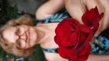 a woman with glasses holds a red rose in her hand