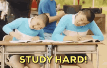 two boys are sitting at desks in a classroom and the words study hard are on the screen .