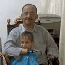 a man in a wheelchair is holding a little boy in his arms .