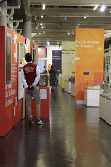 a man in a red jacket stands in front of a sign that says sur le champ du travail