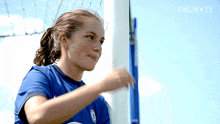 a woman in a blue shirt is standing in front of a soccer goal with the words chelsea tv behind her