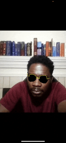 a man wearing sunglasses sits in front of a shelf of books