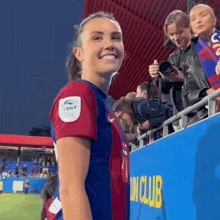 a woman in a soccer uniform is smiling in front of a sign that says ' un club ' on it