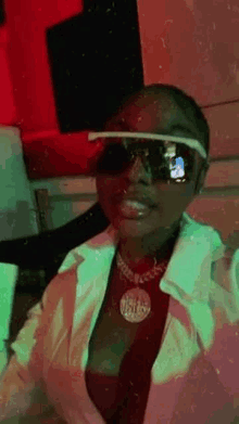 a woman wearing sunglasses , a white jacket , and a red tie is sitting in a dark room .