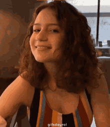 a woman with curly hair wearing a striped tank top smiles