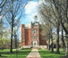 a brick building with a clock tower is surrounded by trees and grass on a sunny day .