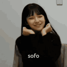 a girl is smiling and making a heart shape with her hands and the word sofo is visible in the corner .