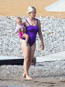 a woman in a purple swimsuit is carrying a baby on the beach