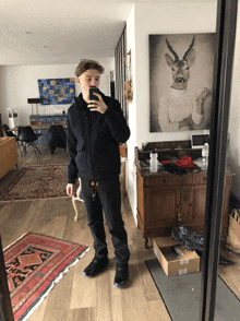 a man taking a selfie in front of a painting of a deer head