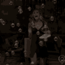 a woman in a black dress is surrounded by bubbles in a dark room