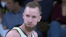 a basketball player with a beard is sitting in the stands during a game and looking at the camera .