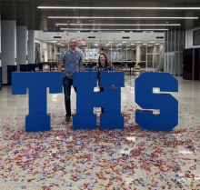 a man and a woman standing in front of a large ths sign surrounded by confetti