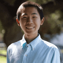 a young man wearing a light blue shirt smiles for the camera