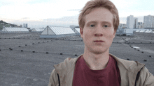 a man in a red shirt is standing on a rooftop with a city in the background