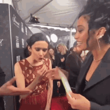 two women are standing next to each other on a red carpet . one of the women is wearing a red dress .