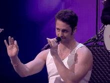 a man in a white tank top singing into a microphone in front of a purple background