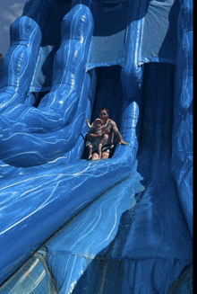 a man and a child are sliding down a blue inflatable slide