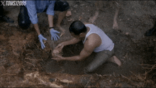 a man in a white tank top is kneeling in the dirt with tomsj 2005 written on the bottom right