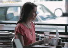 a woman in a red shirt sits at a table with a laptop and a glass of water in front of her