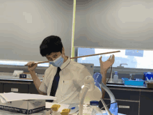 a boy wearing a mask holds a stick in front of a box of sterile examination gloves