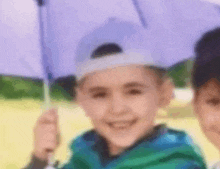 a young boy is holding a purple umbrella while wearing a hat .