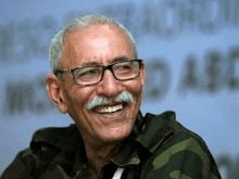 a man with glasses and a mustache is smiling in front of a blurred background