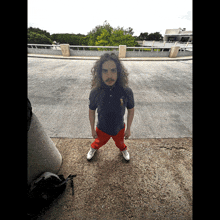 a man with long curly hair wearing a polo shirt and red shorts