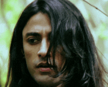 a close up of a man 's face with long dark hair