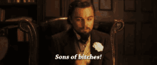 a man in a suit is sitting in a chair with the words sons of bitches above him