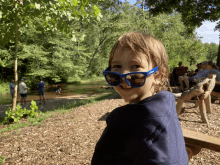 a young boy wearing blue sunglasses is sitting on a bench in front of a river