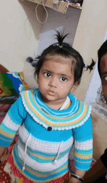 a little girl wearing a blue and white sweater looks at the camera