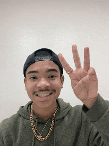 a young man wearing a black hat and a gold chain is giving the peace sign