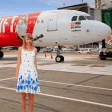 a woman in a blue and white dress is standing in front of a malaysia airbus plane