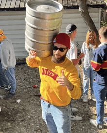 a man wearing a yellow queen sweatshirt is carrying a keg on his shoulder