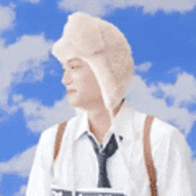 a man wearing a hat and tie is standing in front of a blue sky with clouds .