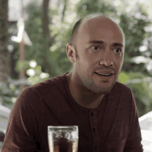 a man in a maroon shirt is sitting at a table with a glass of beer in front of him