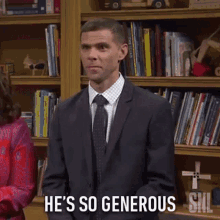 a man in a suit and tie is standing in front of a bookshelf and says he 's so generous