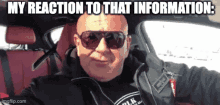 a bald man wearing sunglasses and a black jacket is sitting in a car with the caption " my reaction to that information "