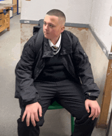 a man in a black jacket and tie is sitting on a green chair